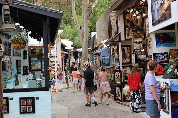Visitors explore local art booths under tall trees at the Sawdust Art Festival 2025 in Laguna Beach, Orange County.